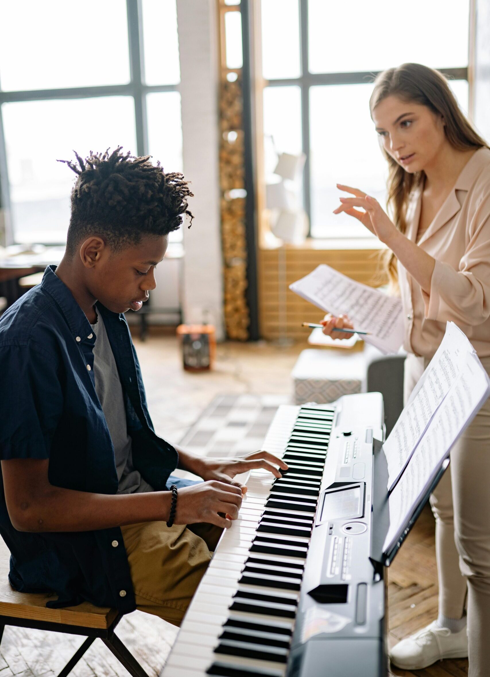 pexels-yankrukov-8520498-min A teenage student plays an electric keyboard while a music teacher offers guidance and holds sheet music.