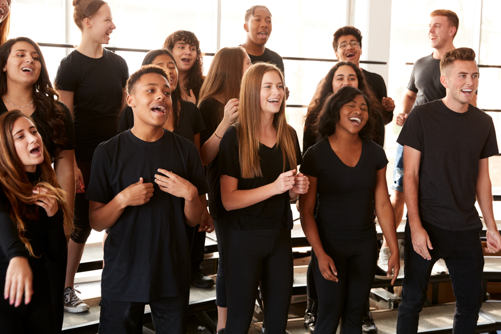 A diverse group of high school students sings together enthusiastically during a choir rehearsal on risers.