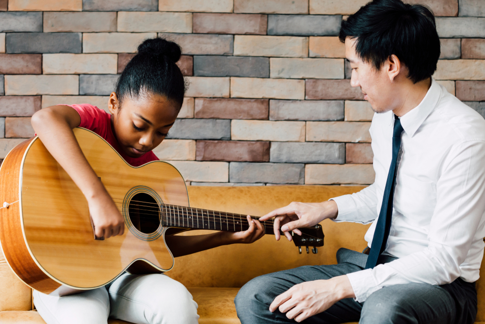 Young,Asian,Male,Teacher,Giving,A,Guitar,Lesson,And,Teaching Young Asian male teacher giving a guitar lesson and teaching.