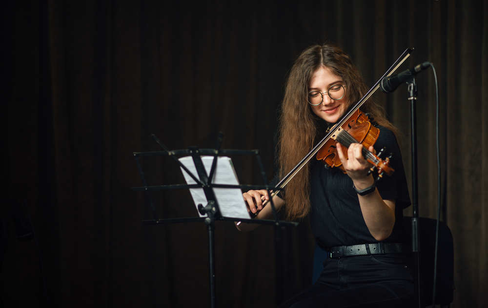 Classical,Musician,Playing,The,Violin,On,Stage A student violinist rehearses confidently on stage, reading sheet music and performing under soft lighting.
