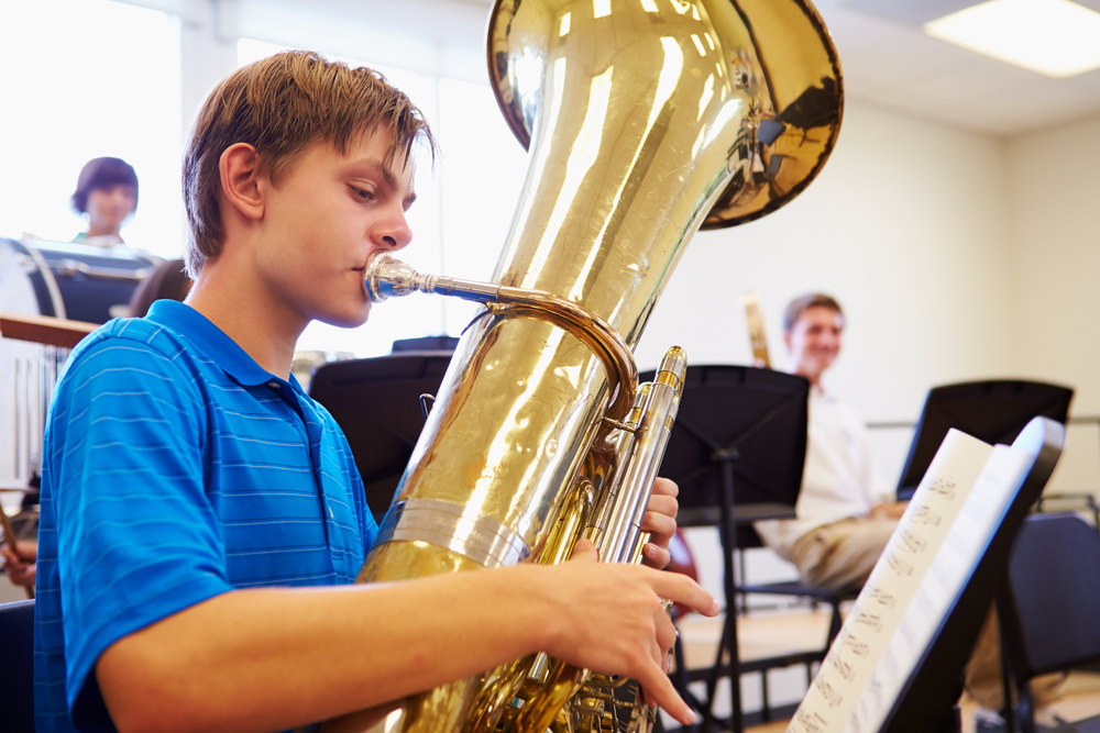 Male,Pupil,Playing,Tuba,In,High,School,Orchestra High school aged boy in blue shirt playing the tuba in orchestra class