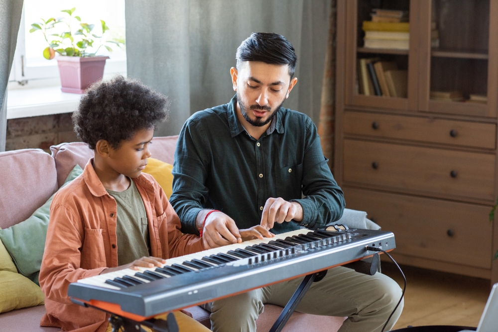 Young,Teacher,Of,Music,Consulting,Little,Schoolboy,About,Playing,Piano A piano teacher gives individualized instruction to a young student during a one-on-one keyboard lesson at home.