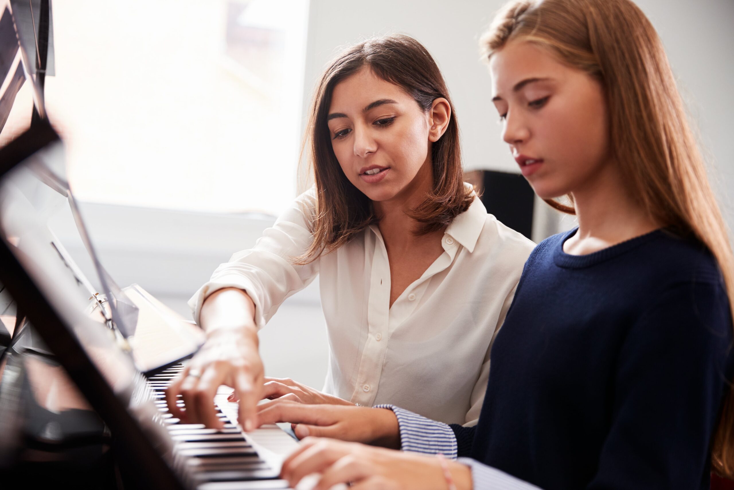 A piano teacher gives personalized instruction to a teen student during a focused one-on-one music lesson.