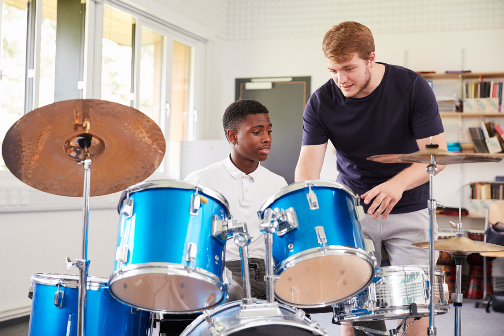 Male,Pupil,With,Teacher,Playing,Drums,In,Music,Lesson A drum instructor guides a student through hands-on practice in a bright, well-equipped music classroom.