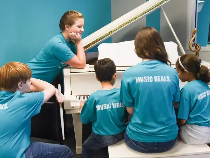 Students sitting at a piano with teacher in music room